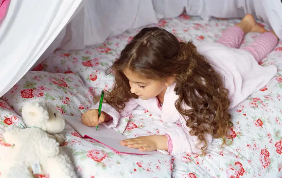 Jente som tegner ligger i seng med blomstrete sengetøy 