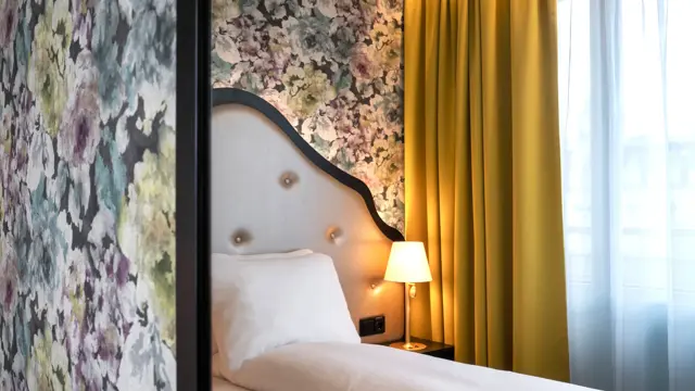 Dobbeltseng med sengegavl, blomstrete tapet og gule gardiner i dobbeltrom på Thon Hotel Cecil