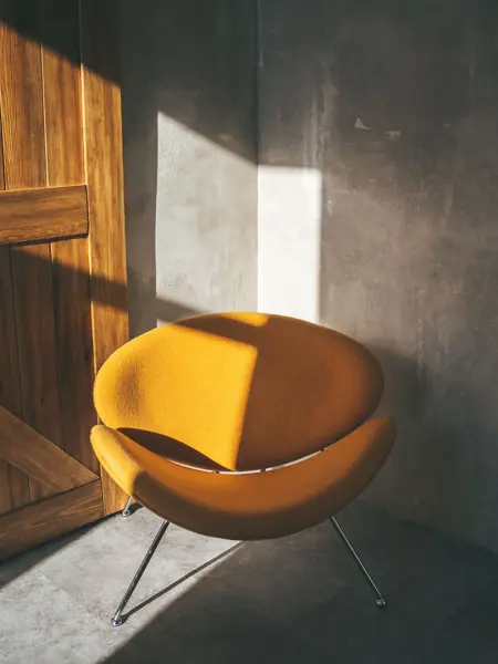 Gul stol i rom i grå betong og med en tredør i bakgrunnen.