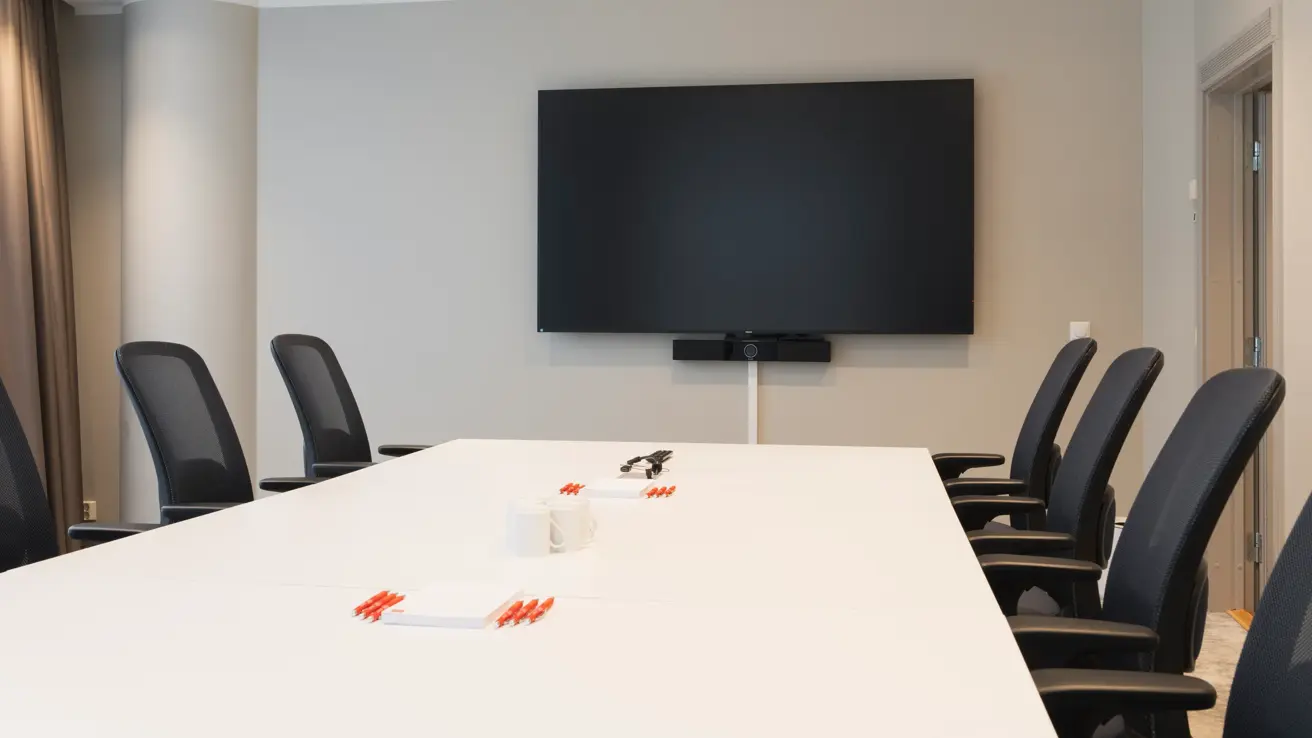 Møterom med langbord, svarte kontorstoler rundt, Tv skjerm på veggen.