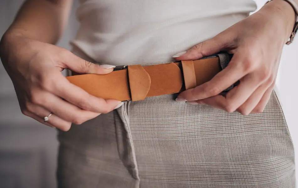 Nærbilde av hender som strammer et belte i brunt semsket skinn