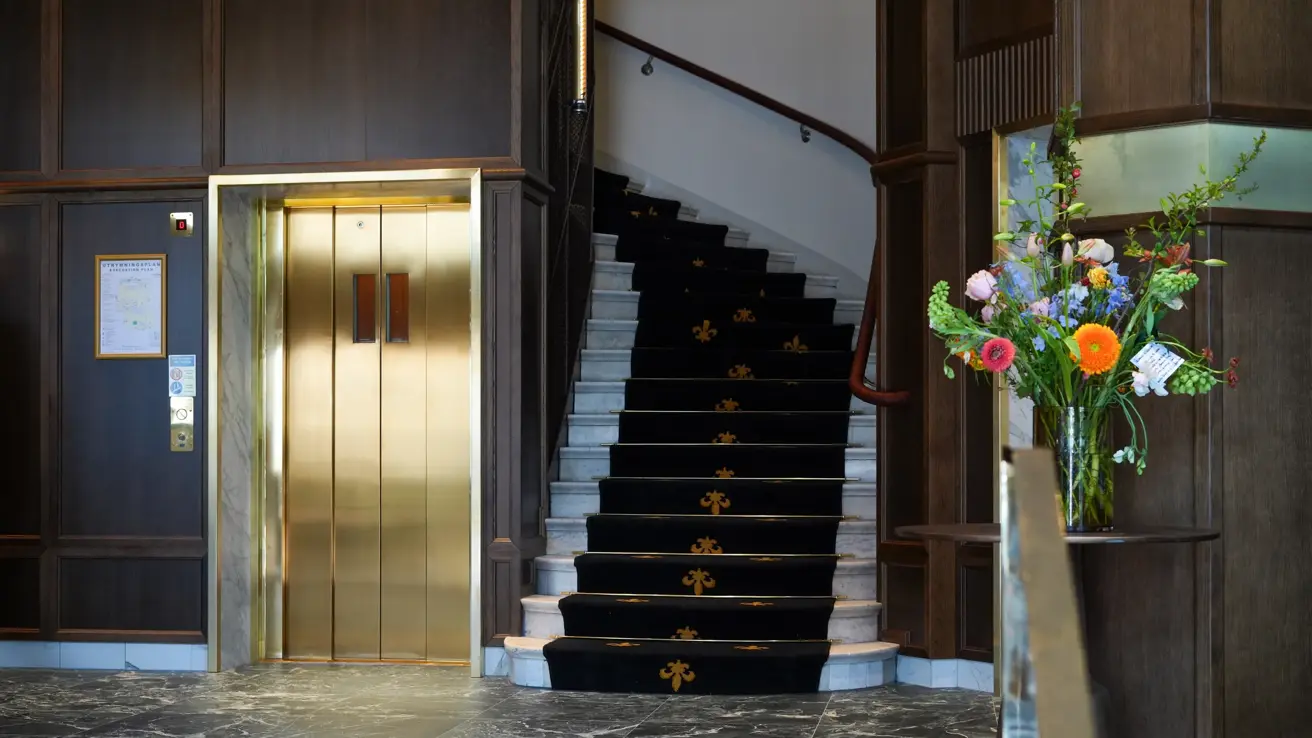 Lobbyområde på Thon Hotel Vasa, med heis, trapp og fargerik blomsterbukett på et bord