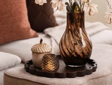 Et brunt fat med en telysholder, en skål formet som en nøtt og en vase med blomster.