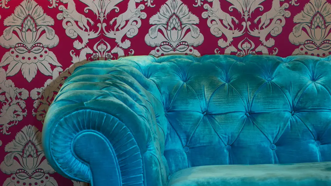 Detaljbilde av fargerik sofa inntil en tapsert vegg og gammelt bilde på vegge i lobbyen på Thon Hotel cecil