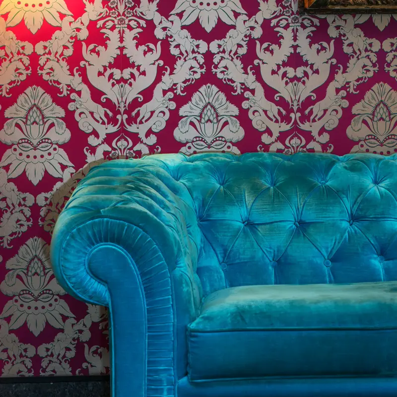 Detaljbilde av fargerik sofa inntil en tapsert vegg og gammelt bilde på vegge i lobbyen på Thon Hotel cecil