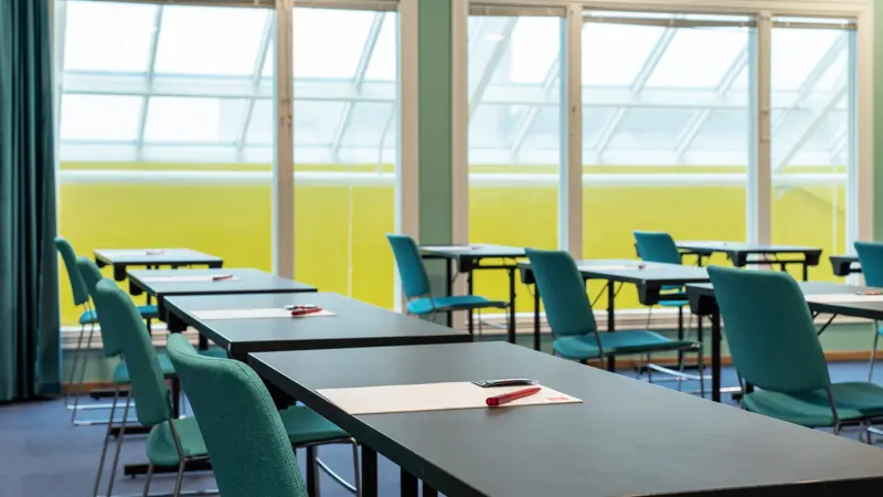 Konferanserom, klasseromoppsett, vindu, turkise stoler, svarte bord. 