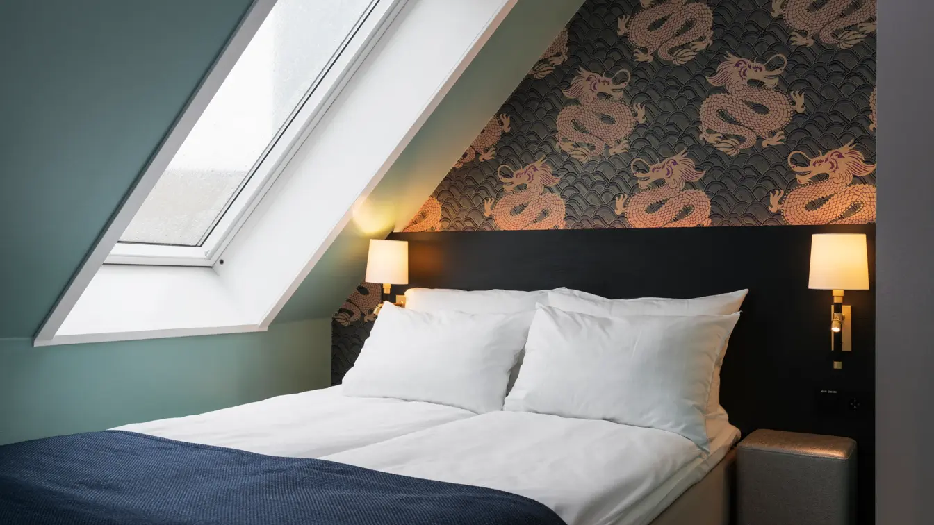 Dobbeltseng med skråtak og vindu med dragetapet på suite på Thon hotel Terminus i Oslo sentrum nær Jernbanetorget
