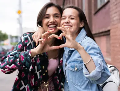 Outdoors fashion portrait young pretty best girls friends in friendly hug. Walking at the city. Posing at the street. Positive emotions