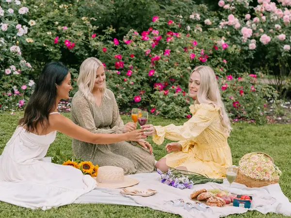 Tre damer som har piknik i en hage