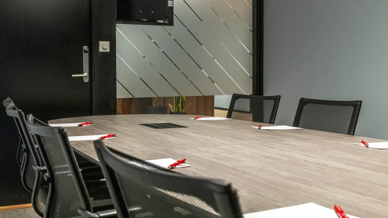 Detaljbilde av møterom med kontorstoler, penn og papir på bordet.