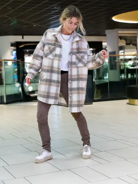 Ung kvinne som poserer i rutete skjortejakke og brune bukser