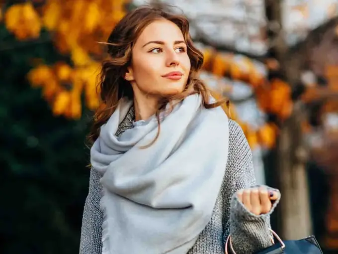 dame med grått skjerf går ute med høstløv i bakgrunn