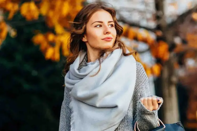 dame med grått skjerf går ute med høstløv i bakgrunn