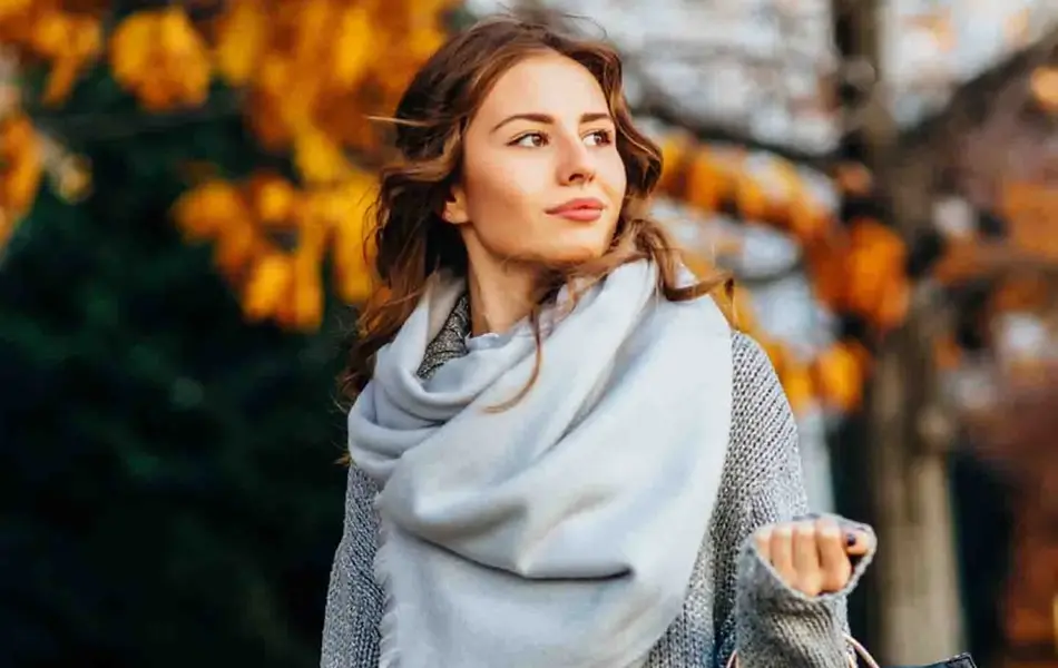 dame med grått skjerf går ute med høstløv i bakgrunn