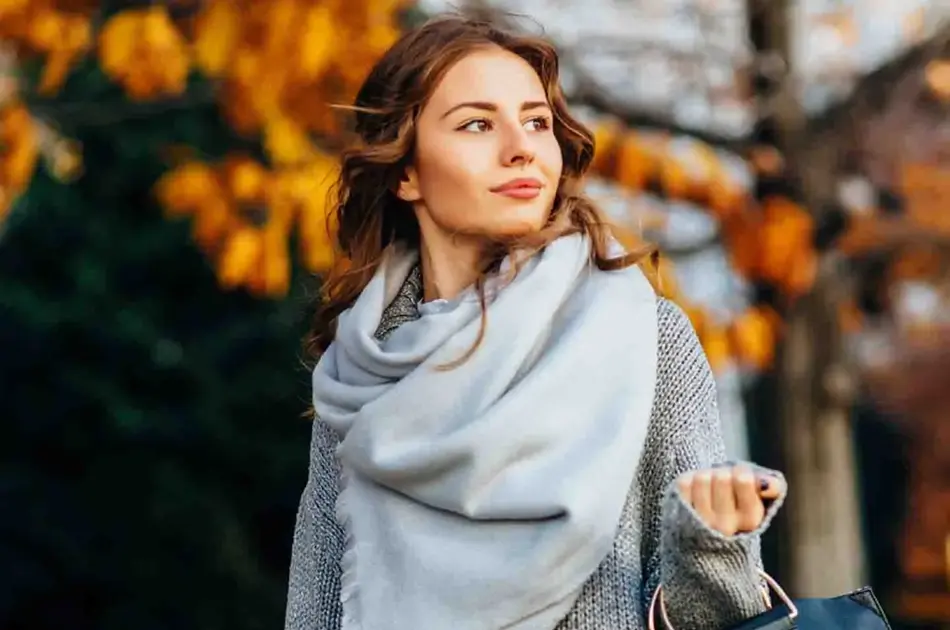 dame med grått skjerf går ute med høstløv i bakgrunn