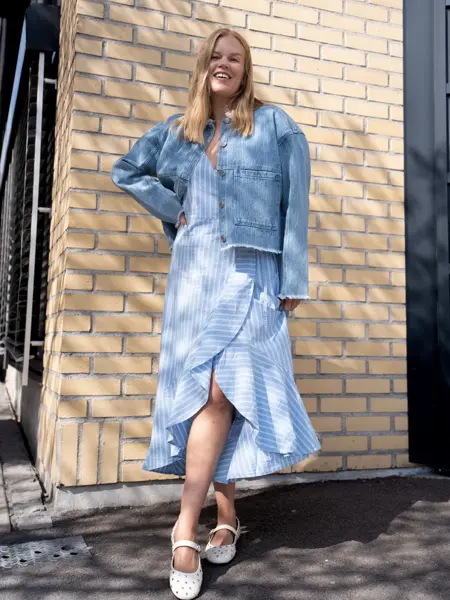 Dame med lyselå og hvit stripete omslagskjole, halvlang, hvite ballerinasko og olajakke