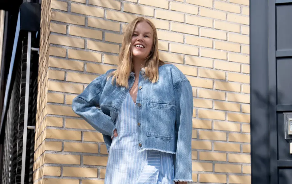 Dame med lyselå og hvit stripete omslagskjole, halvlang, hvite ballerinasko og olajakke