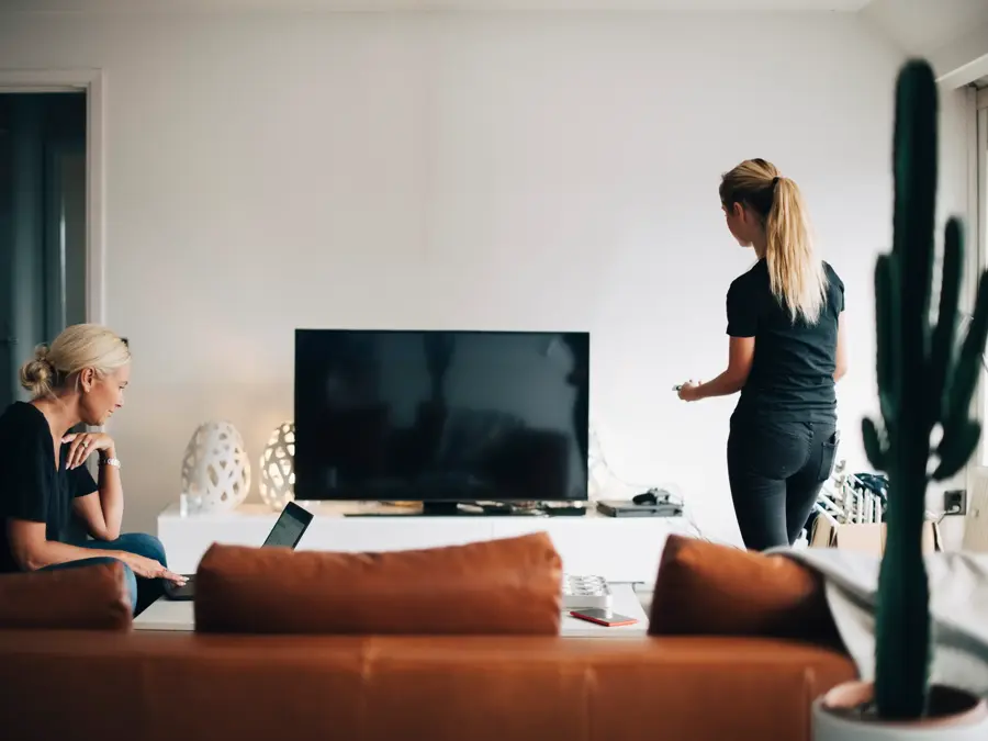 En dame bruker pc og en dame ser på tv 