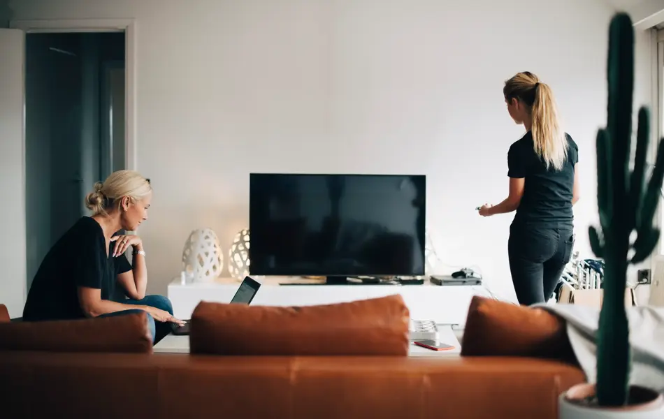 En dame bruker pc og en dame ser på tv 