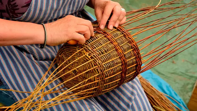 Kvinne med forkle som sitter og fletter en kurv