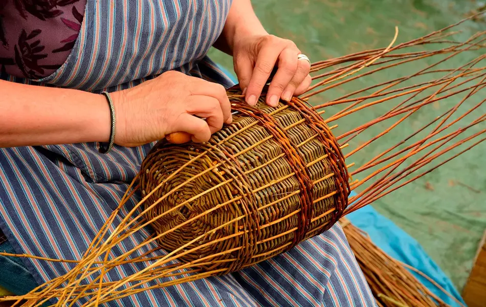 Kvinne med forkle som sitter og fletter en kurv