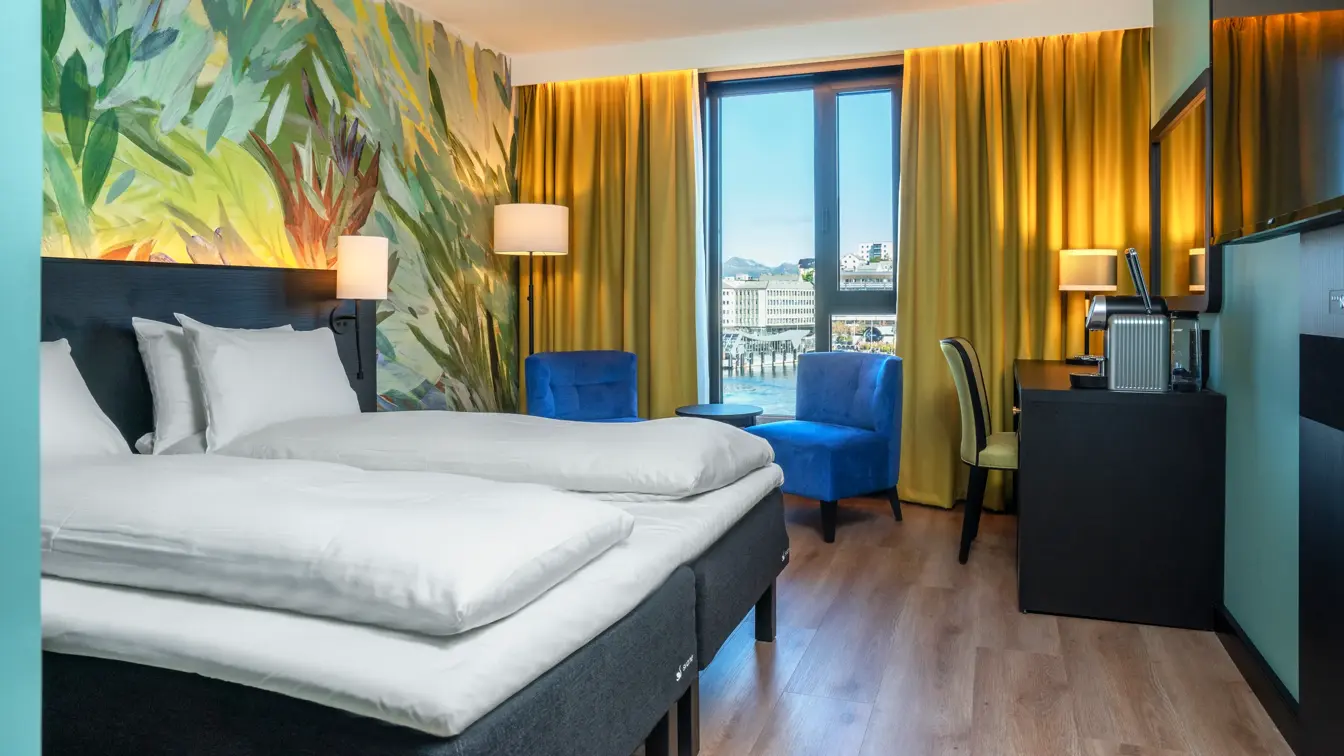 Skrivebord, TV, dobbeltseng, to blå lenestoler, skrivebord, gul stol