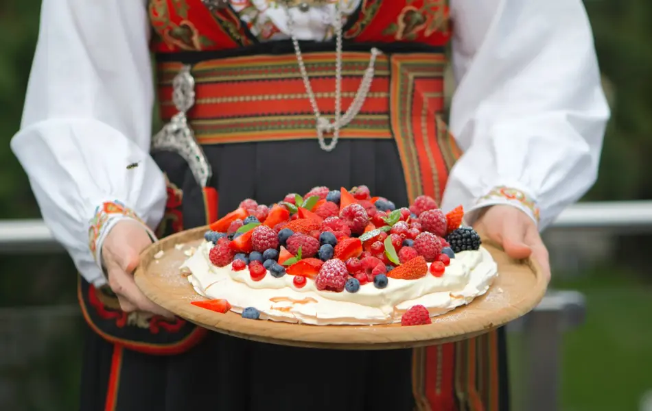 Dame i bunad holder et kakefat med Pavlova fylt med krem og bær
