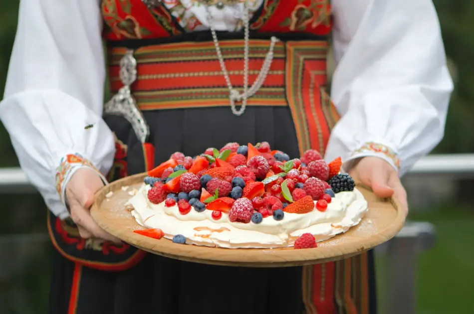 Dame i bunad holder et kakefat med Pavlova fylt med krem og bær