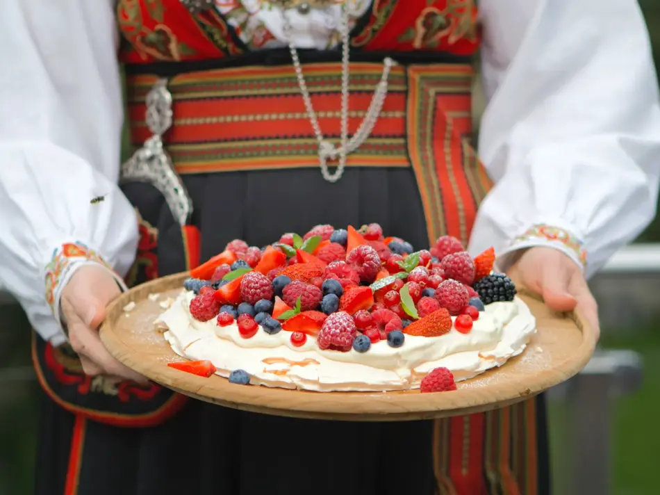 Dame i bunad holder et kakefat med Pavlova fylt med krem og bær