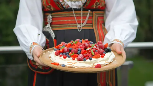 Dame i bunad holder et kakefat med Pavlova fylt med krem og bær