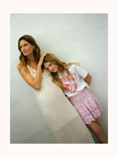 Dame står ute med heklet lang kjole, jente med rosa skjørt og t-skjorte.