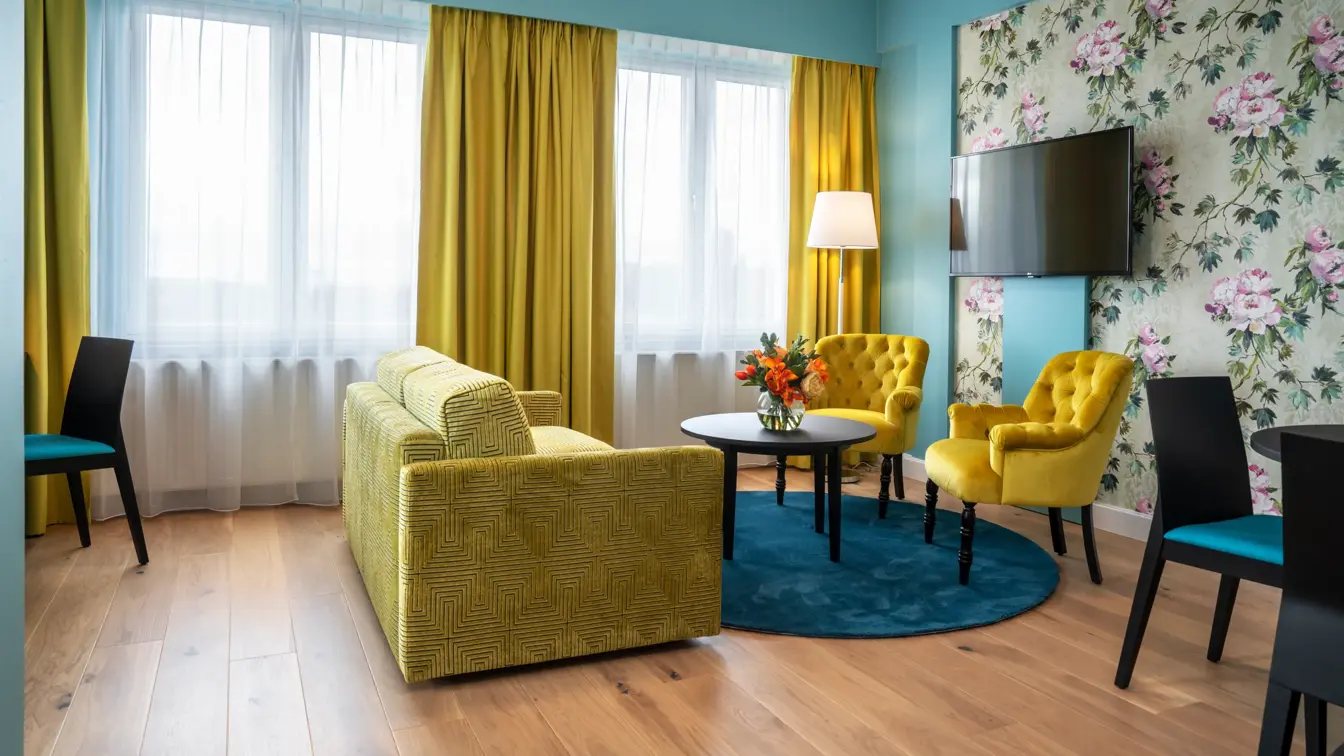 Blomstrete tapetvegg, blå vegg, peis, gul sofa, to gule stoler, blått teppe, spisebord med fire stoler, vindu fra gulv til tak, gule gardiner, to speil på veggene, Tv-skjerm