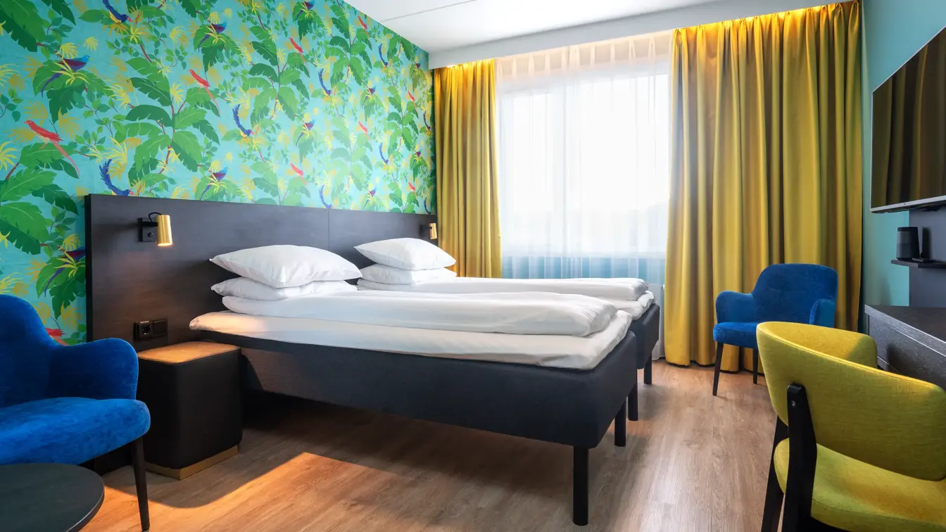 Grønn tapetvegg med mønster, gule gardiner, dobbeltseng, parkettgulv, blå stol, skrivebord, vindu, gul stol