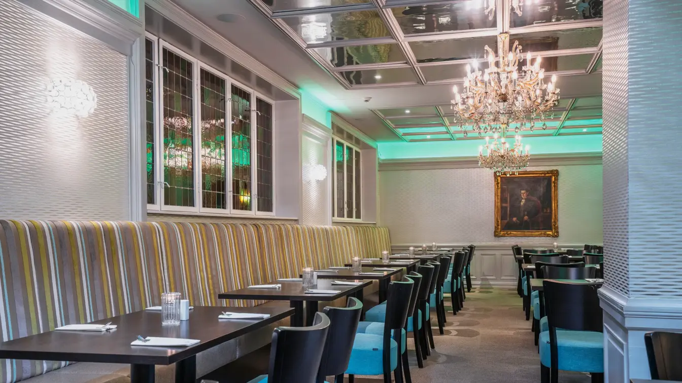 Svarte spisebord, blå stoler, hvite vegger, vindu, lysekrone i tak. 