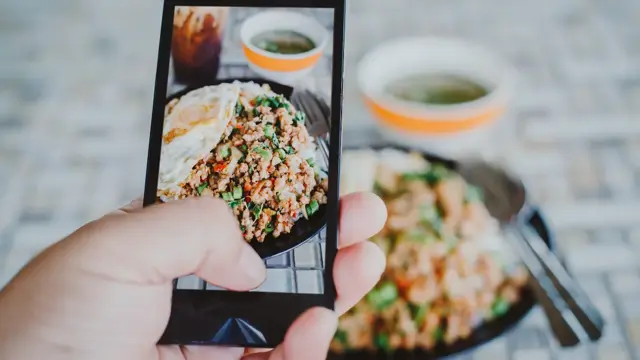 Hånd med mobiltelefon som tar bilde av mat