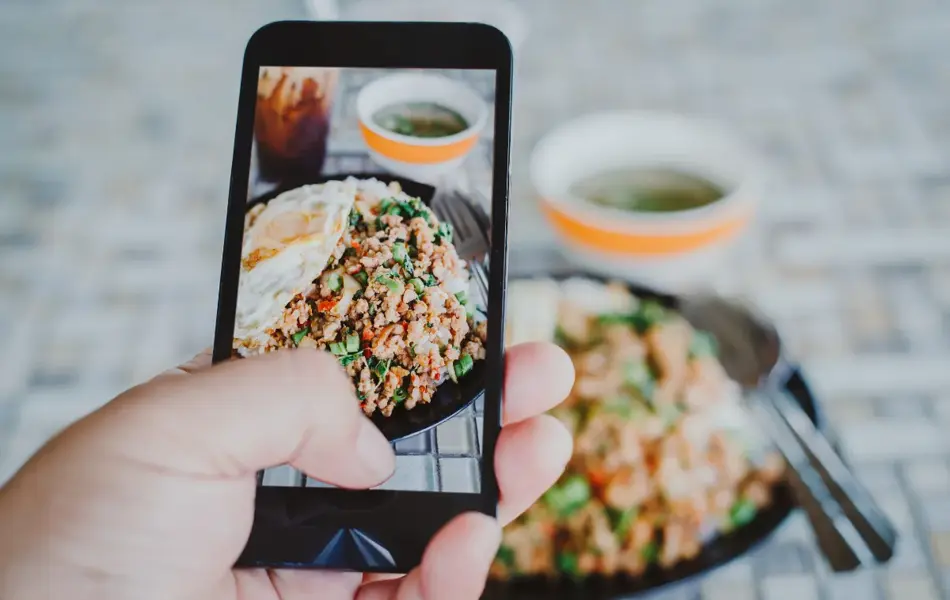 Hånd med mobiltelefon som tar bilde av mat