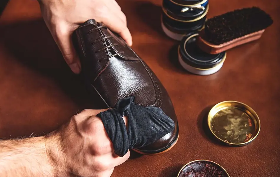 Nærbilde av hender som pusser sko, med diverse skopusserutstyr på bord med dyp rød overflate. Foto til artikkel om gavetips til farsdag.