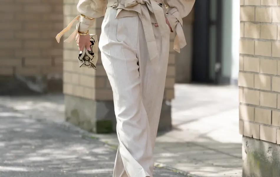 Dame i beige bukse, sandaler, hatt og beige jakke