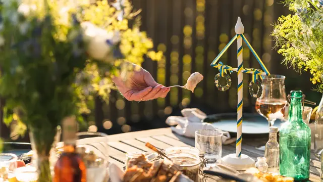 En mann plukker opp et stykke sild fra en krukke fra et midtsommerbord