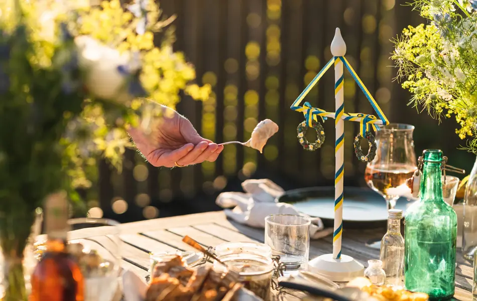 En mann plukker opp et stykke sild fra en krukke fra et midtsommerbord