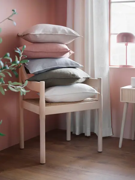 Stol med flere puter på i et rosa rom med gardiner.