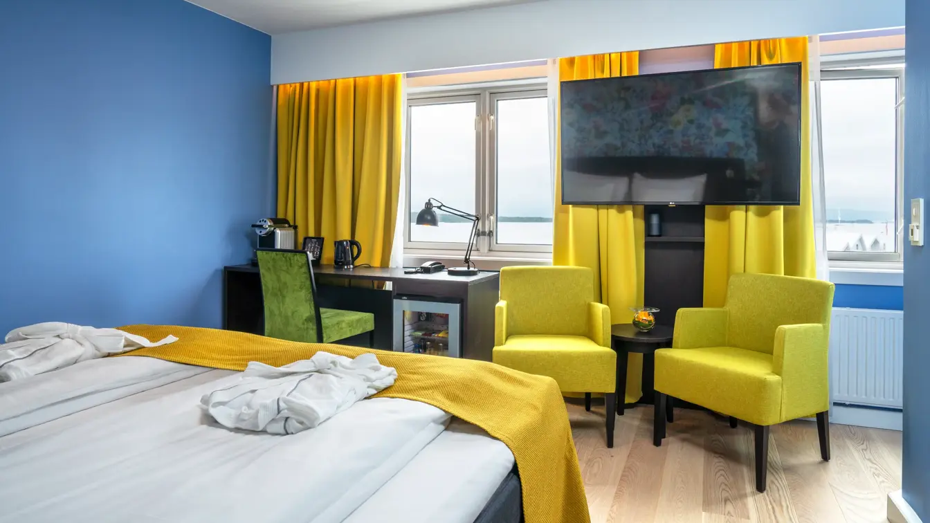 Dobbeltseng med morgenkåper på, stoler og TV