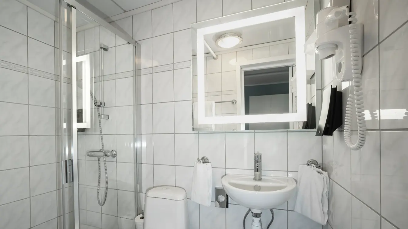 Toalett, vask, dusj, hvite veggfliser, hårføner, speil. 