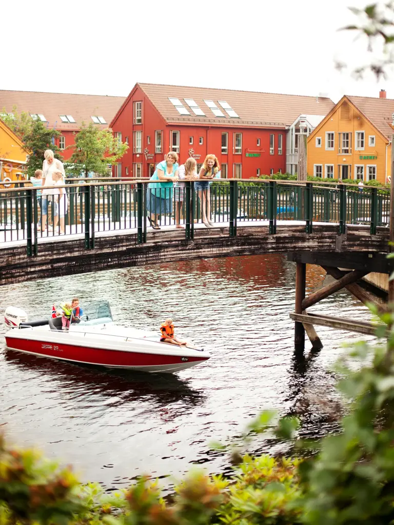 Bru ved Fiskebrygga i Kristiansand. På brua står det voksne og barn. Under brua kjører en båt.