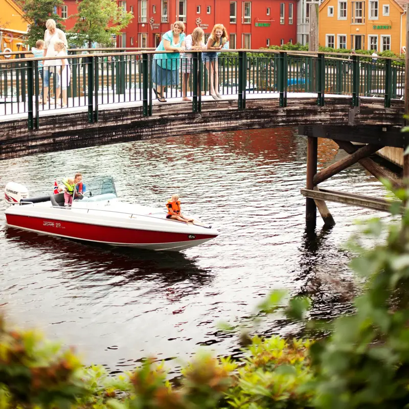 Bru ved Fiskebrygga i Kristiansand. På brua står det voksne og barn. Under brua kjører en båt.