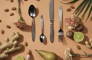 Bestikk i rustfritt stål omgitt av frukt, blomster og planter.