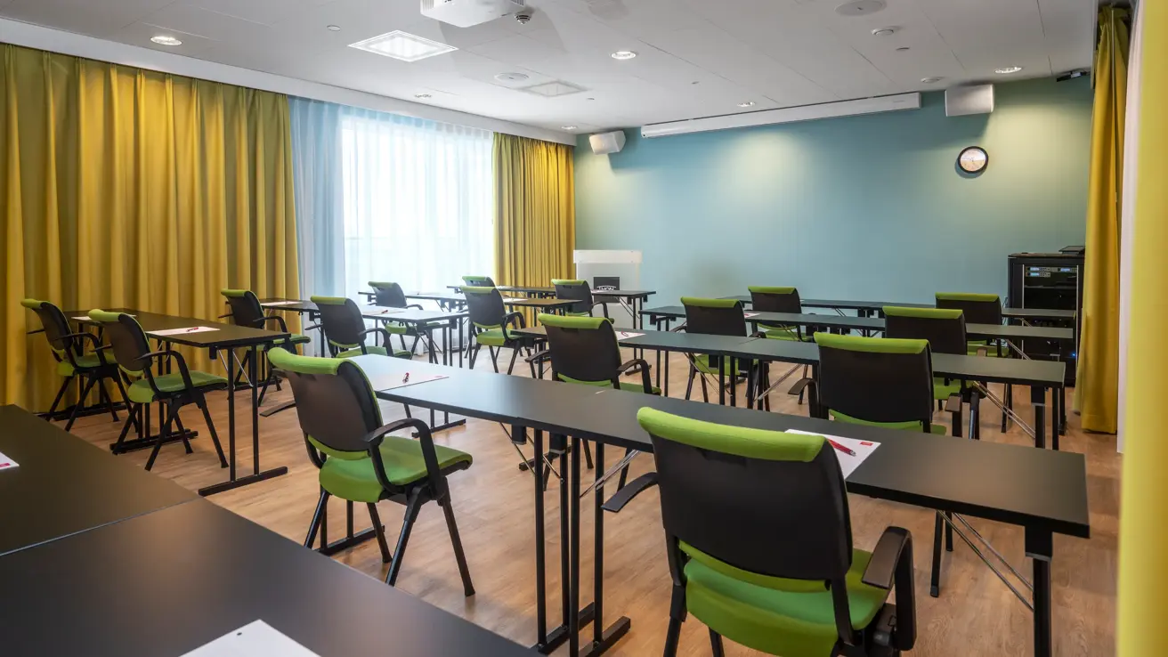 Konferanserom, klasseromoppsett, 1m avstand, grønne stoler, gulv vegg, gule gardiner.