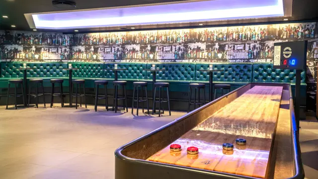 shuffleboard, grønn skinnsofa, runde høye bord med barkrakker. 