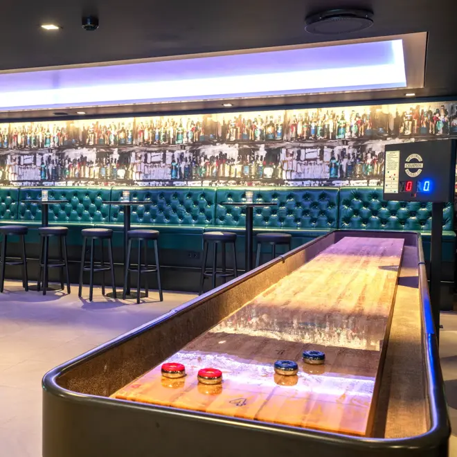 shuffleboard, grønn skinnsofa, runde høye bord med barkrakker. 