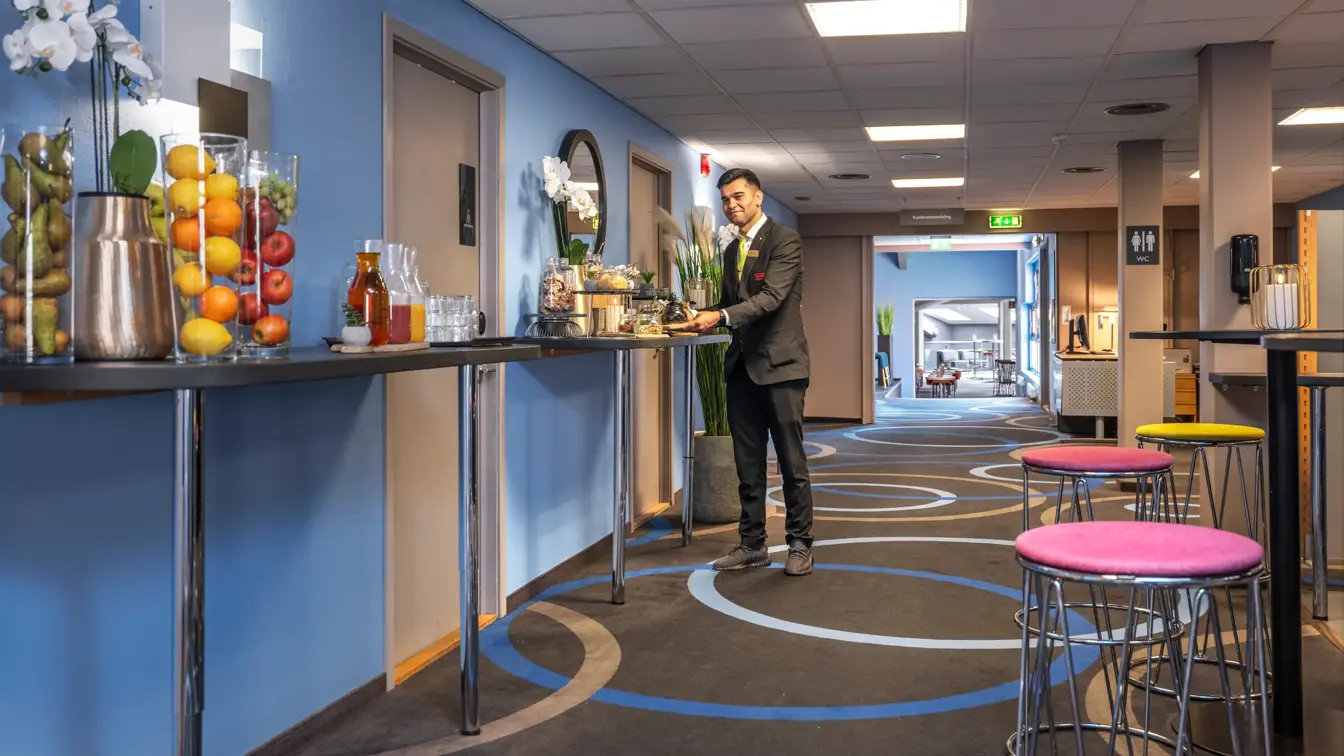 Konferansevert klargjør pausebuffet på høybord i konferanseområde.